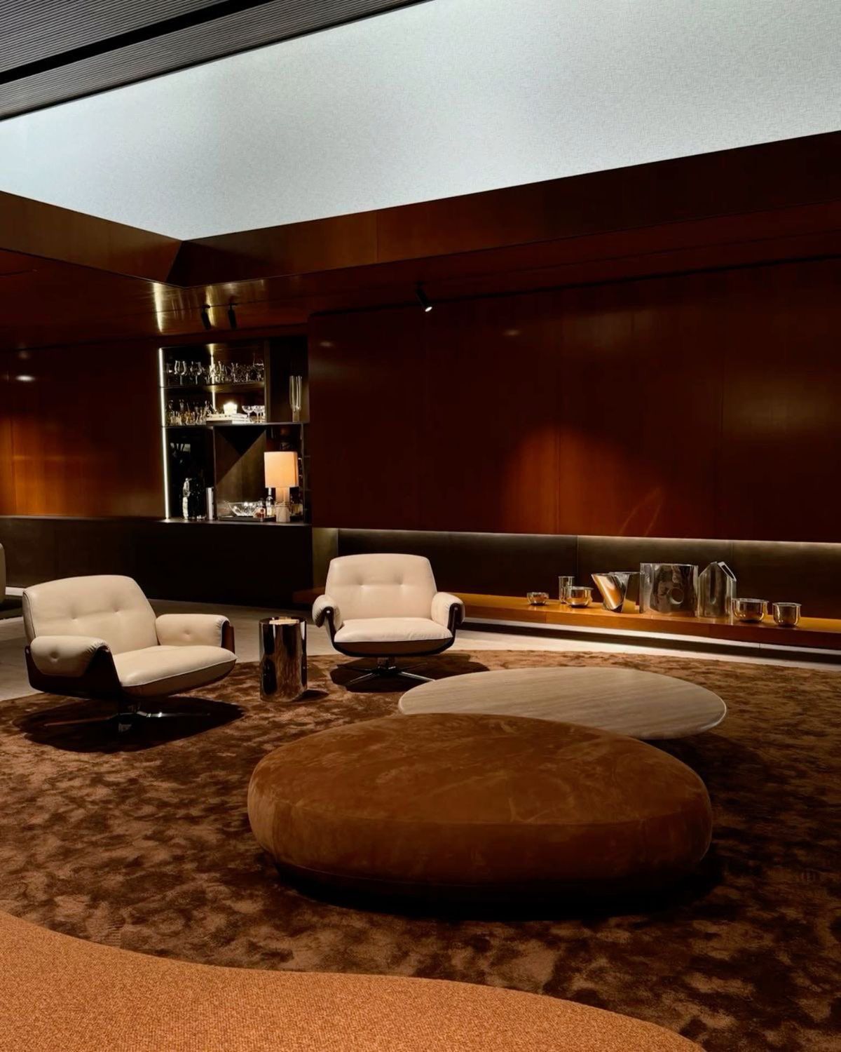 Walnut-panelled lounge with cream swivel chairs, a suede ottoman and a travertine coffee table
